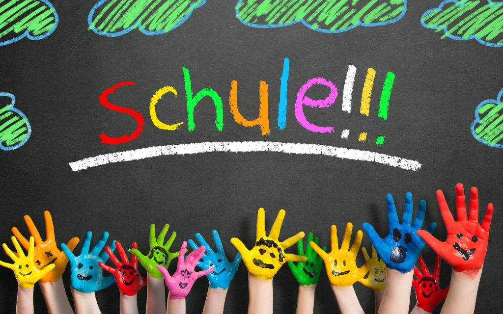 napis szkoła po niemiecku i pomalowane farbą dłonie dzieci