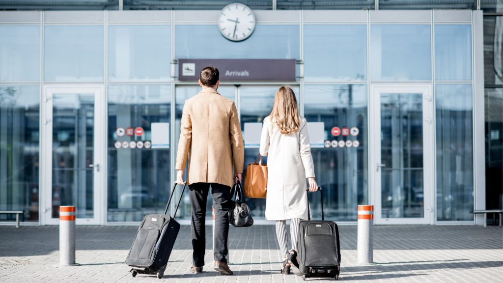 жінка і чоловік стоять перед входом в аеропорт і тримають валізи в руках