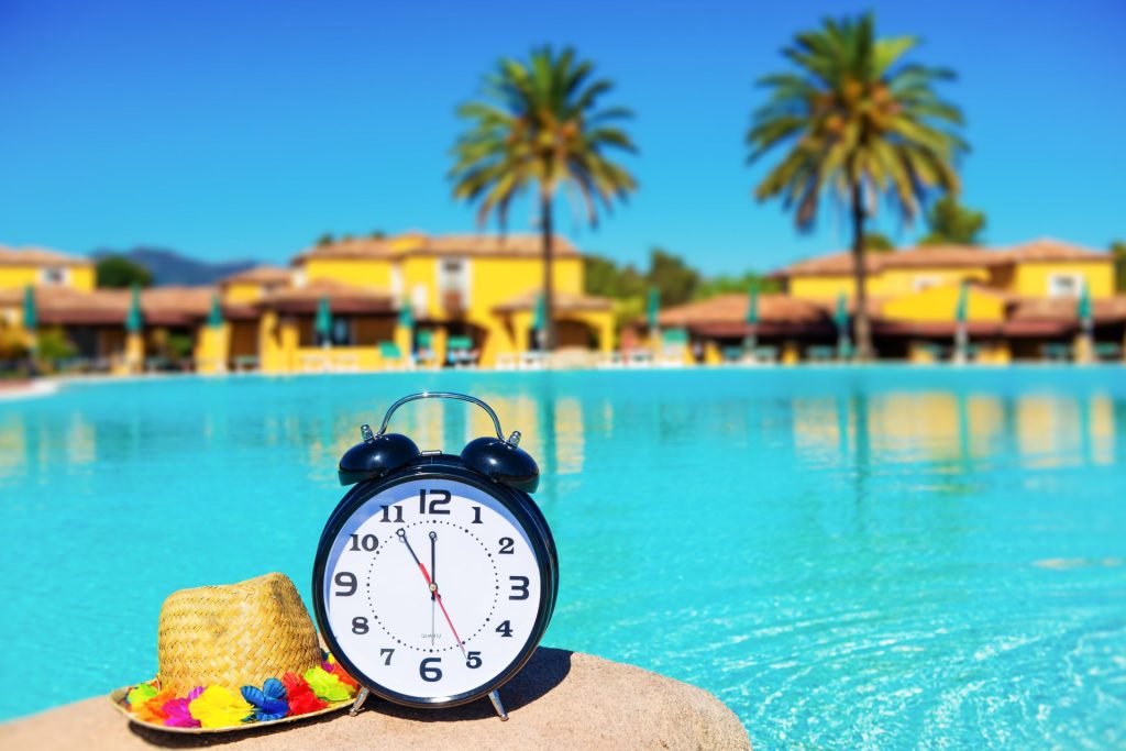 a clock and a hat lie in front of the pool and palm trees