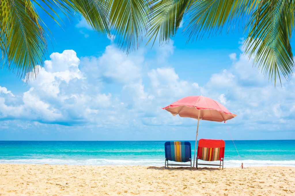 beach, sea, slightly cloudy sky, palm trees, two sun loungers and a sun umbrella