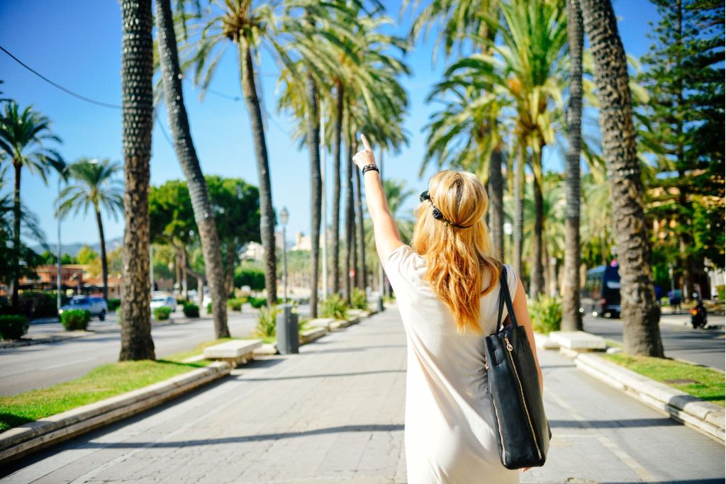 girl on vacation shows at the palm trees and walks along the street