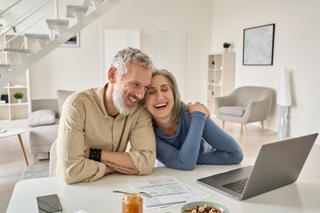 Kobieta i mężczyzna w średnim wieku, śmiejący się patrząc na laptopa 