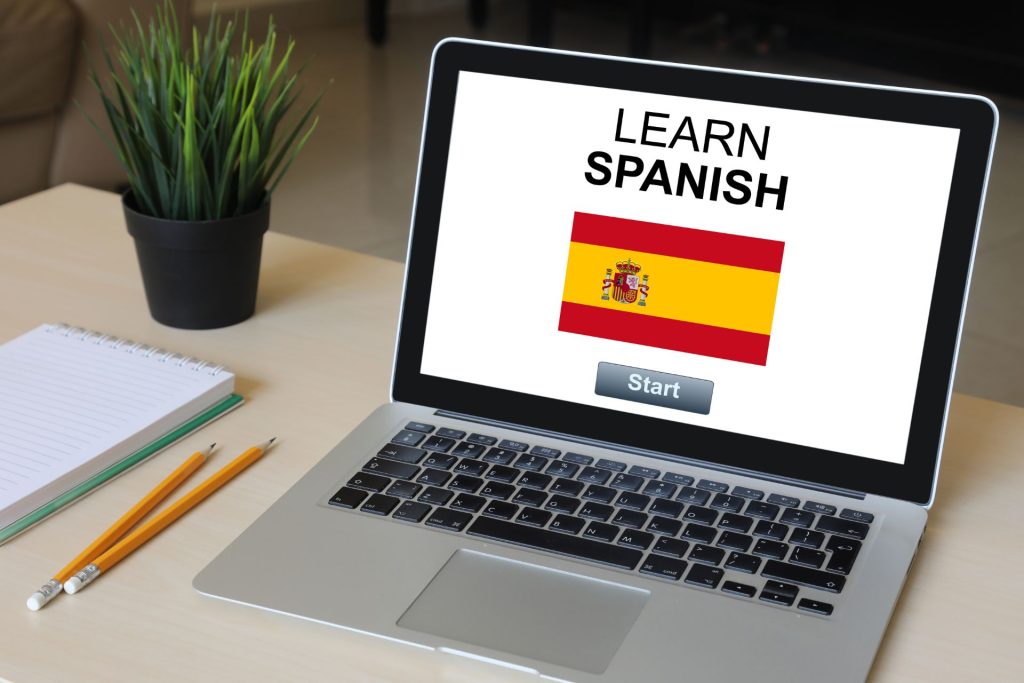 otwarty laptop leżący na biurku, z napisem na ekranie "LEARN SPANISH" oraz z flagą hiszpańską