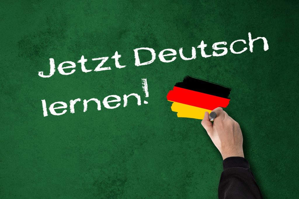 pisząca dłoń po tablicy kredowej i napis "jetzt deutsch lernen!"