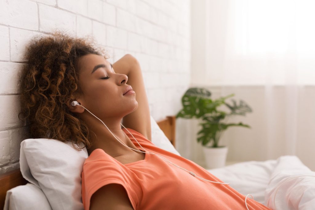 kobieta leżąca na łóżku w słuchawkach w uszach, z zamkniętymi oczami