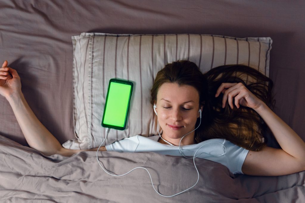 kobieta ze słuchawkami w uszach leżąca na łóżku